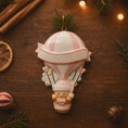 Load image into Gallery viewer, Personalized baby first Christmas ornament featuring a soft pastel pink hot air balloon design with a sweet baby character inside the basket. Handwritten baby name and year or Baby’s First Christmas text displayed on the balloon. Smooth resin finish with gentle glitter accents, nursery themed colors, lightweight structure, mostly 2D ornament with raised 3D details on the front only, designed for baby Christmas tree decor and keepsake gifting.