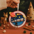 Load image into Gallery viewer, Decorative ornament with space theme featuring a telescope, planet, and stars, held by a hand.