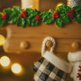 Load image into Gallery viewer, Decorative gingerbread house with holly leaves and berries on a blurred lights background