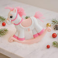 Load image into Gallery viewer, Pink and white rocking horse ornament with decorative elements on a snowy background