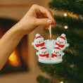 Load image into Gallery viewer, Hand holding a Christmas ornament with four snowmen in Santa hats against a blurred Christmas tree background.