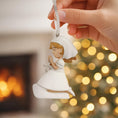 Load image into Gallery viewer, Decorative angel ornament held by a hand with a blurred Christmas tree and fireplace in the background.