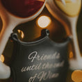 Load image into Gallery viewer, Black koozie with 'Friends until the end of wine' text, blurred wine bottles in the background