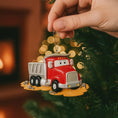 Load image into Gallery viewer, Red truck ornament with a face, held by a hand against a Christmas tree background.
