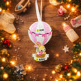 Load image into Gallery viewer, A personalized baby girl ornament featuring a cute bunny riding a pastel pink hot air balloon. Soft pink and white tones with delicate bow details create a sweet and cozy look. Handwritten personalization includes baby name and year. Mostly 2D ornament with raised 3D details on the front only, lightweight and easy to hang, perfect for baby first Christmas, nursery decor, and toddler keepsakes.