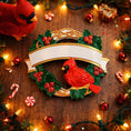 Load image into Gallery viewer, Personalized cardinal wreath ornament featuring a vibrant red cardinal bird surrounded by green holly leaves and red berries. Designed with a smooth glossy finish and a raised 3D front with a flat back for easy hanging. Includes free handwritten personalization with one name and year displayed on the banner at the top. Styled in a warm festive holiday setting with soft Christmas lights candy details and seasonal decor. A meaningful Christmas tree ornament symbolizing remembrance love and connection perfect