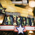 Load image into Gallery viewer, A resin Army tank ornament in bold yellow features a cartoon style military tank with detailed black tracks and raised cannon, camouflage green ARMY lettering across the front, a star accent and American flag inspired base, surrounded by snow texture and festive holiday elements, with handwritten personalization showing one name on the left banner and the year on the right banner, designed as a mostly 2D ornament with raised 3D details on the front only for lightweight Christmas tree decor.