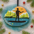 Load image into Gallery viewer, Decorative ornament with paddleboard design on a textured surface with Christmas decorations.