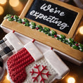 Load image into Gallery viewer, Decorative baby announcement sign with mittens and snowflake design, surrounded by festive lights.