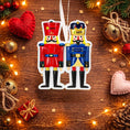 Load image into Gallery viewer, Festive close up of a personalized nutcracker couple ornament featuring two classic nutcracker figures in red and blue uniforms with custom name details. Designed for couples, partners, siblings, or loved ones, this ornament symbolizes balance, tradition, and togetherness. A timeless Christmas keepsake ideal for tree decor, holiday gifting, and celebrating meaningful bonds.