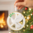 Load image into Gallery viewer, Decorative Christmas ornament with a dove and peace symbol, held by a hand against a festive background.