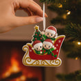 Load image into Gallery viewer, Christmas ornament with three children in a sleigh, held by a hand in front of a lit fireplace.