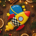 Load image into Gallery viewer, Colorful rocket-shaped Christmas ornament on a wooden surface with festive decorations.