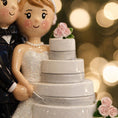 Load image into Gallery viewer, Wedding cake topper with bride and groom figurines against a blurred lights background