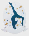 Load image into Gallery viewer, Personalized gymnastics Christmas ornament featuring an oval white design with a navy blue gymnast silhouette performing a handstand pose, surrounded by gold and blue star accents, customizable year displayed on the upper area, customizable name space on the bottom banner, smooth glossy finish with raised 3D front details and flat 2D back, white hanging ribbon, photographed on a soft pink snowy holiday background with winter greenery, festive ornaments, and warm seasonal styling.