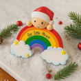 Load image into Gallery viewer, Decorative ornament with a rainbow, cloud, and baby figure with a Santa hat on a snowy background.