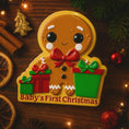 Load image into Gallery viewer, Gingerbread man ornament with 'Baby's First Christmas' text on a wooden background with festive decorations.