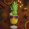 Load image into Gallery viewer, Pineapple with sunglasses and a name tag on a wooden surface with Christmas decorations.