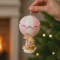 Load image into Gallery viewer, A personalized baby girl ornament featuring a cute bunny riding a pastel pink hot air balloon. Soft pink and white tones with delicate bow details create a sweet and cozy look. Handwritten personalization includes baby name and year. Mostly 2D ornament with raised 3D details on the front only, lightweight and easy to hang, perfect for baby first Christmas, nursery decor, and toddler keepsakes.