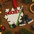 Load image into Gallery viewer, Hockey-themed Christmas ornament with skates and stick on a wooden surface.