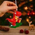 Load image into Gallery viewer, Colorful dinosaur themed Christmas ornament designed for kids, featuring a playful character and bright cheerful tones. Set in a cozy holiday scene, this ornament brings fun and imagination to children’s Christmas tree decor. Designed to be personalized, making it a special keepsake for kids who love dinosaurs and playful holiday decorations.