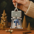 Load image into Gallery viewer, Decorative ornament of a person on a chair with a laptop, held by a hand against a festive background.