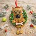 Load image into Gallery viewer, Dog-shaped Christmas ornament with a wreath on a sandy background with toys and decorations.
