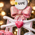 Load image into Gallery viewer, Personalized Baby Girl First Christmas Ornament featuring a dimensional 3D front design with pink glitter bow, heart charms, and hanging cloud detail. The baby’s name is added on the top circle and the year on the cloud, creating a meaningful keepsake. Soft pink tones, layered hearts reading Baby’s First Christmas, and festive holiday accents make it perfect for newborn girl gifts, baby shower presents, and treasured Christmas tree memories.