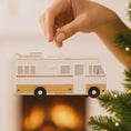 Load image into Gallery viewer, Hand holding a Christmas ornament shaped like a camper van against a blurred festive background