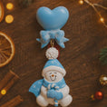 Load image into Gallery viewer, Decorative snowman ornament with blue hat and heart on a wooden surface with Christmas decorations.