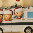 Load image into Gallery viewer, Christmas ornament of a family in a car with Santa hats on a blurred light background