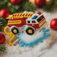 Load image into Gallery viewer, Colorful toy fire truck ornament on a snowy background with Christmas decorations.