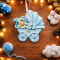 Load image into Gallery viewer, Personalized baby boy Christmas ornament featuring a light blue stroller with glitter details and a smiling baby wearing a blue nightcap. Custom name appears on the top and year on the bottom, making it a perfect Baby’s First Christmas keepsake. This blue resin holiday ornament is ideal for newborn boys, baby shower gifts, and celebrating a special first Christmas memory.