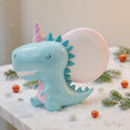 Load image into Gallery viewer, Cute dinosaur-shaped night light with a unicorn horn on a snowy surface with Christmas decorations.