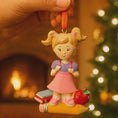Load image into Gallery viewer, Decorative ornament of a girl with books and an apple against a warm, festive background.