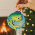 Load image into Gallery viewer, Decorative fish ornament held by a hand with a blurred festive background