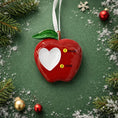 Load image into Gallery viewer, Red apple-shaped ornament with a white heart on a green background with Christmas decorations.