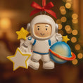 Load image into Gallery viewer, Personalized astronaut Christmas ornament featuring a detailed 3D front design with a smiling space explorer holding a colorful planet and bright yellow stars. The childâs name is added on the suit and the year is written on the star for a custom touch. This space themed ornament is perfect for kids who love rockets, planets, and outer space dreams. A fun and meaningful holiday keepsake for future astronauts and little space lovers.