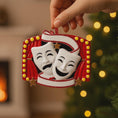 Load image into Gallery viewer, Decorative Christmas ornament with theater masks held by a hand against a blurred festive background.