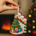 Load image into Gallery viewer, Christmas ornament with family around a tree, held by a hand with a blurred festive background.
