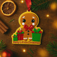 Load image into Gallery viewer, Gingerbread ornament with 'Baby's First Christmas' text on a wooden surface with festive decorations.