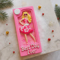 Load image into Gallery viewer, A vibrant pink fashion doll ornament with a retro camera-frame look and floral dress, perfect for holiday trees. Features bright colors, playful style, and a customizable area for adding a name or short text. Designed as a fun keepsake for kids and collectors who love bold, glamorous ornaments. Ideal for Christmas décor, stocking stuffers, and memorable seasonal gifting.