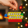 Load image into Gallery viewer, Personalized Master Builder Christmas ornament featuring a raised 3D front with colorful building block design and bold lettering. The ornament has a flat 2D back for easy hanging and durability. Bright primary colors and playful block details make it perfect for kids who love building toys. Personalization includes name and year, added by hand, making it a fun and meaningful holiday keepsake for children and young builders.