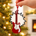 Load image into Gallery viewer, Red guitar-shaped Christmas ornament held by a hand against a festive background with lights and a fireplace.