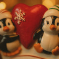 Load image into Gallery viewer, Two penguin figurines with a red heart and snowflake decoration on a blurred background.