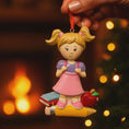 Load image into Gallery viewer, Decorative ornament of a girl with books and an apple against a warm, blurred background.