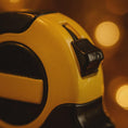 Load image into Gallery viewer, Close-up of a yellow and black object with blurred lights in the background