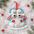 Load image into Gallery viewer, Two polar bear ornaments in blue hats and scarves on a snowy background with Christmas decorations.