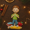 Load image into Gallery viewer, Decorative figurine of a boy with books and an apple on a pencil, surrounded by Christmas decorations.