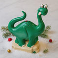 Load image into Gallery viewer, Green dinosaur toy on a snowy background with Christmas decorations
